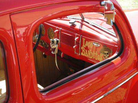 1998 Ford Crown Victoria - Interior dash of a red hot rod seen through the window, with chrome gauges and a gold Loco Banditos skull graphic on the dash.