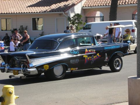 1998 Ford Crown Victoria - black 1957 Chevrolet gasser with raised front end, slick rear tires and Axle Twister lettering sits on a street near a fire hydrant.