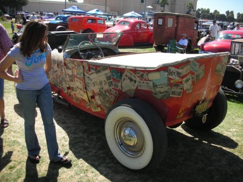 1998 Ford Crown Victoria - red roadster pickup whose bodywork is covered in a black-and-white photo collage, with a woman in a Ford shirt admiring it at a show.