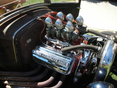 1998 Ford Crown Victoria - chrome Fireplite Eight flathead-style V8 with multiple polished carburetors sits in a patina hot rod engine bay at a show.
