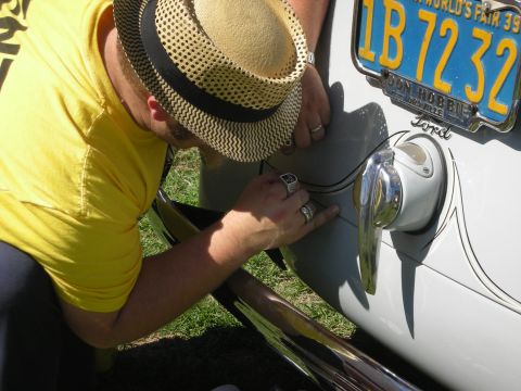 1998 Ford Crown Victoria - man in a straw fedora pinstripes the side of a white Ford near a yellow 1939 New York Worlds Fair license plate.