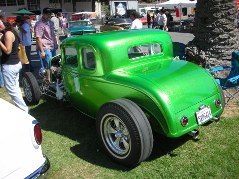 1998 Ford Crown Victoria - Rear three-quarter view of a metallic-green 1932-style five-window hot rod coupe with chrome wheels and exposed engine at a car show.