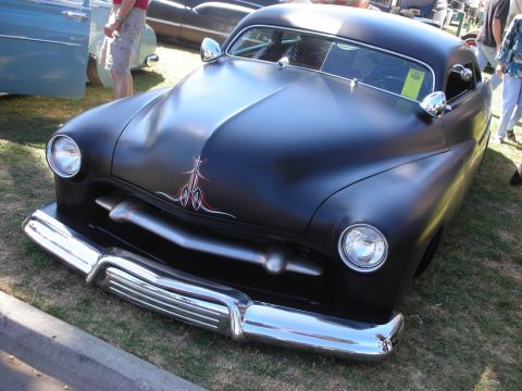 1998 Ford Crown Victoria - flat-black chopped lead-sled custom with red and white hood pinstriping and a wide chrome bumper sits low on a show field.