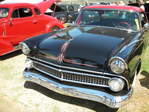 1998 Ford Crown Victoria - glossy black mid-fifties Ford hardtop with a red roof and hood pinstriping shines beside a red coupe on a show field.