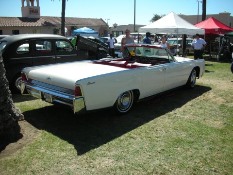 1998 Ford Crown Victoria - white early-sixties Lincoln Continental convertible with red interior sits top-down on grass under show tents and palms.