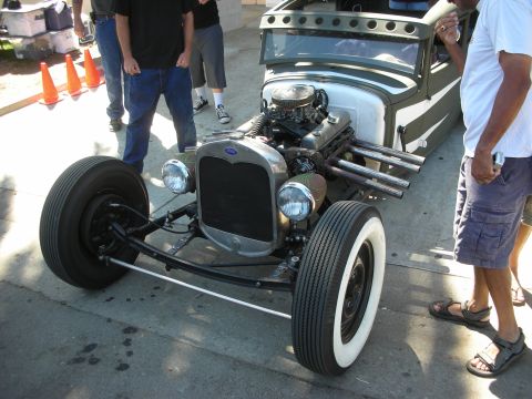 1998 Ford Crown Victoria - bare-frame Ford rat rod with exposed V8, open zoomie headers and whitewall tires sits on a street as onlookers gather.