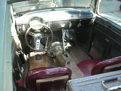 1998 Ford Crown Victoria - stripped interior of a vintage hot rod shows a wood-rimmed steering wheel, drilled spokes, pinstriped dash, and worn maroon vinyl seats.