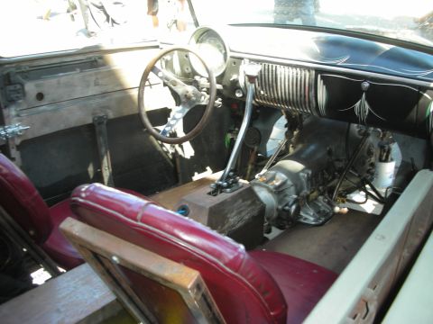 1998 Ford Crown Victoria - hot rod's bare interior features a tall floor-mounted shifter, finned dashboard trim, and tattered red leather bench seating.