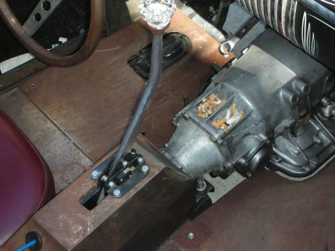 1998 Ford Crown Victoria - close-up shows a hot rod's exposed manual transmission, a chrome shift lever topped with a clear faceted glass knob, over a rusty floor.