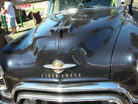1998 Ford Crown Victoria - detail of a black car's hood shows the chrome Oldsmobile globe emblem above raised OLDSMOBILE block lettering.