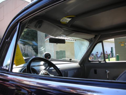 1998 Ford Crown Victoria - Looking through a classic car's side window reveals the steering wheel, a round gauge on the dash, and onlookers at a car show outside.
