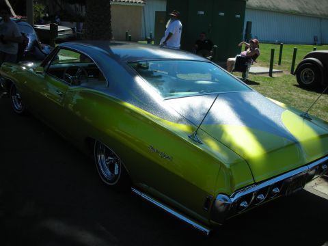1998 Ford Crown Victoria - lime-green metalflake custom fastback coupe with chrome wheels gleams in sunlight, viewed from the rear three-quarter at a car show.