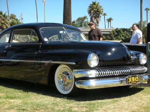 1998 Ford Crown Victoria - front quarter of a black chopped Mercury custom shows its toothy chrome grille, frenched headlight, and wide whitewall tire on grass.