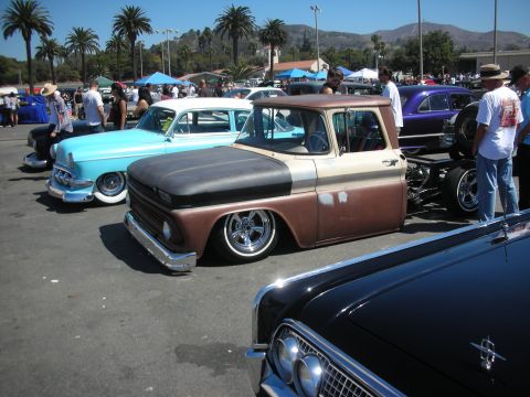 1998 Ford Crown Victoria - lowered two-tone brown and tan early-1960s Chevrolet C10 pickup parked among classic cars at a sunny outdoor show.