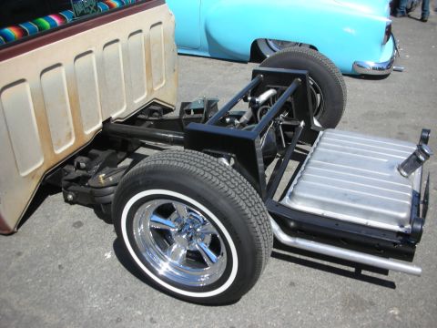 1998 Ford Crown Victoria - stripped hot rod rolling chassis showing the frame, suspension, fuel tank and whitewall tire with chrome wheel at a car show.