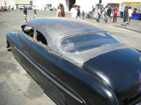 1998 Ford Crown Victoria - black chopped lead-sled custom coupe with weathered patina roof and a window decal, parked at a crowded car show.