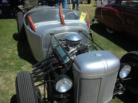 1998 Ford Crown Victoria - Front three-quarter view of a silver roadster hot rod showing its V8 engine, chrome air cleaner and headlights on grass.