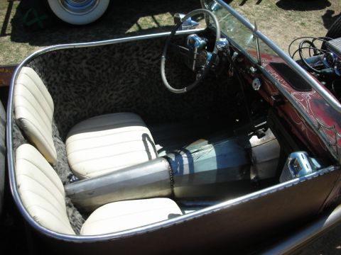 1998 Ford Crown Victoria - Hot rod cockpit showing white tuck-and-roll bench seats, leopard-print panels, banjo steering wheel and a driveshaft.