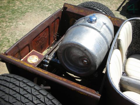 1998 Ford Crown Victoria - polished aluminum keg used as a fuel tank mounted in the rusty patina bed of a rat rod pickup on grass.
