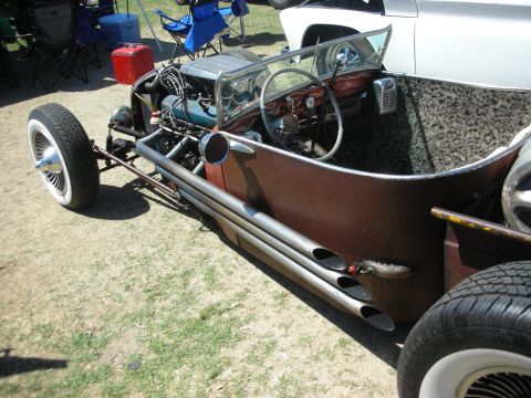 1998 Ford Crown Victoria - Side profile of a very low rat rod roadster with patina body, exposed engine, side exhaust pipes and whitewall tires.