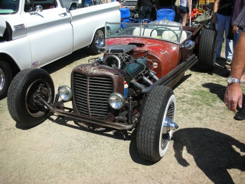 1998 Ford Crown Victoria - brown patina rat rod roadster with exposed V8, pinstriping, twin headlights and whitewall tires displayed on grass.