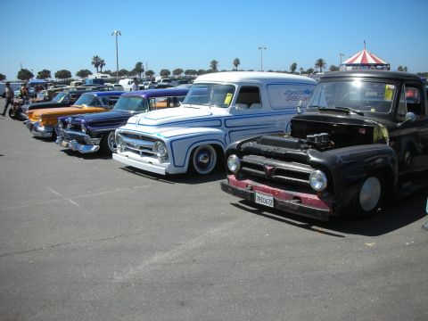 1998 Ford Crown Victoria - row of slammed classic vehicles including a white panel truck and black pickup lined up at a parking-lot car show.