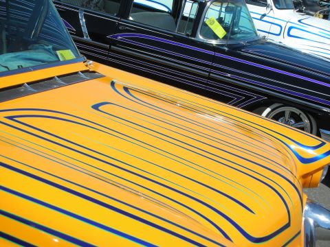1998 Ford Crown Victoria - Close-up of a yellow custom car hood covered in elaborate blue pinstripe scallops beside a black pinstriped car.