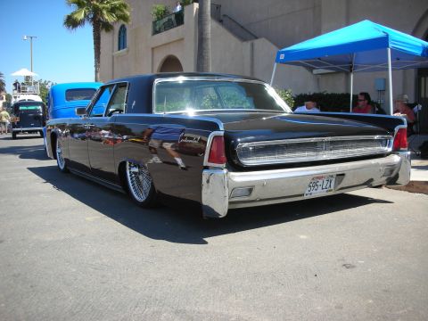 1998 Ford Crown Victoria - black lowered Lincoln Continental sedan with chrome wire wheels parked rear-quarter at an outdoor car show under blue canopies.