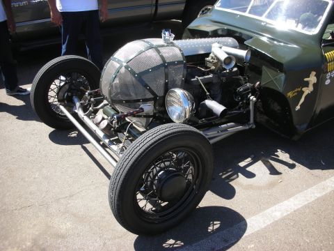 1998 Ford Crown Victoria - Front three-quarter view of an olive-green hot rod roadster with a screened mesh nose, black wire wheels and exposed engine.