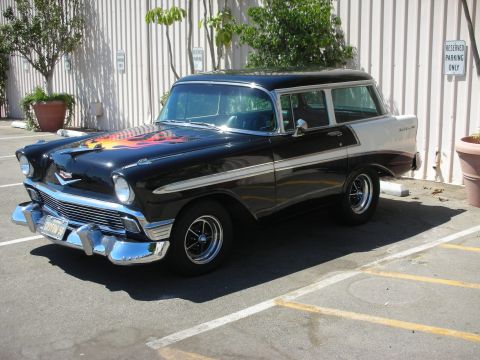 1998 Ford Crown Victoria - black two-door station wagon with flames on the hood and chrome trim parked front-quarter against a metal building.