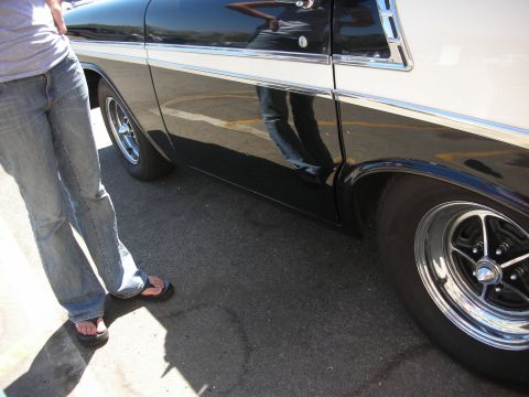 1998 Ford Crown Victoria - person in jeans and sandals stands beside the lower flank and chrome rear wheel of a black flamed station wagon in a lot.