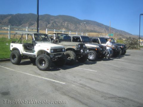 1987 Suzuki Samurai - A line of off-road vehicles, including a white Suzuki Samurai and multiple Jeeps, are parked in a lot.