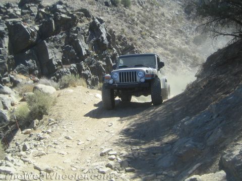 1987 Suzuki Samurai - Jeep Wrangler navigates a dusty, rocky trail in a mountainous area.