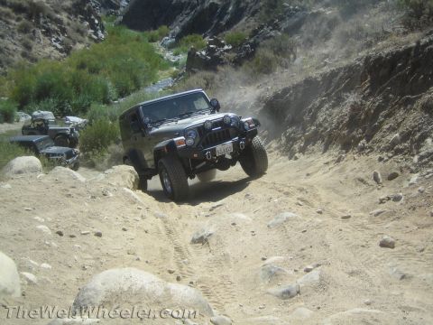 1987 Suzuki Samurai - Several Jeeps navigate a challenging off-road trail in a dry, mountainous area.