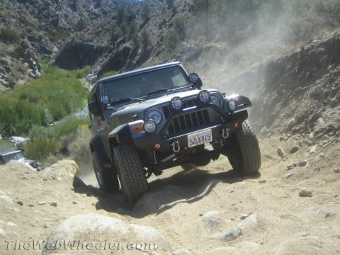 1987 Suzuki Samurai - A Jeep Wrangler navigates a challenging off-road trail, kicking up dust.
