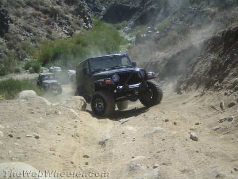 1987 Suzuki Samurai - Off-roading in a canyon with multiple Jeeps kicking up dust on the trail.