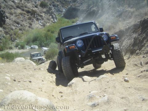 1987 Suzuki Samurai - Two Jeeps navigate a challenging off-road trail, kicking up dust as they go.