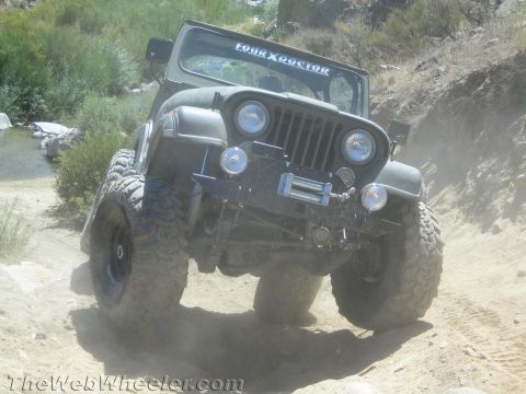 1987 Suzuki Samurai - A Jeep CJ-5 navigates a dusty, off-road trail near a stream.