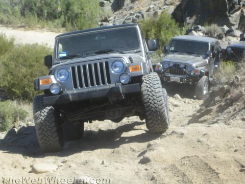 1987 Suzuki Samurai - Several Jeeps navigate a challenging off-road trail with rocky terrain and sparse vegetation.