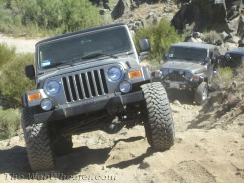 1987 Suzuki Samurai - Multiple Jeeps navigate a rocky, off-road trail under a clear sky.
