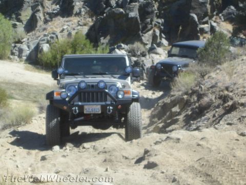 1987 Suzuki Samurai - Two Jeeps navigate a challenging off-road trail with rocky terrain and sparse vegetation.