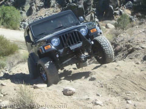 1987 Suzuki Samurai - A black Jeep Wrangler navigates a challenging rocky and dusty trail, demonstrating its off-road capabilities.