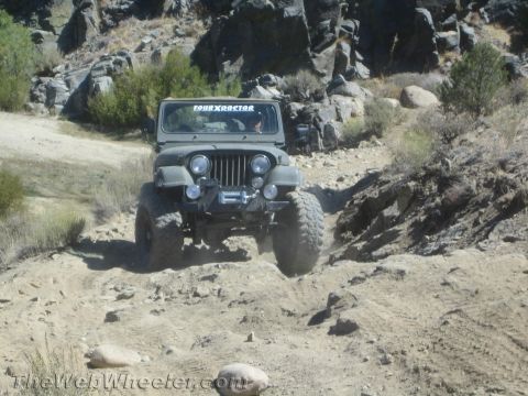 1987 Suzuki Samurai - A Jeep CJ-5 navigates a challenging off-road trail with rocky terrain and sparse vegetation.