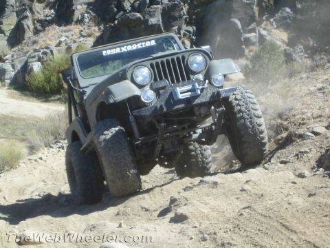 1987 Suzuki Samurai - Olive green Jeep CJ-7 navigates a rocky, dusty trail with aggressive off-road tires.