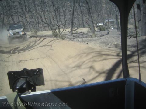 1987 Suzuki Samurai - Jeeps navigate a dusty trail in a wooded area with burnt trees.