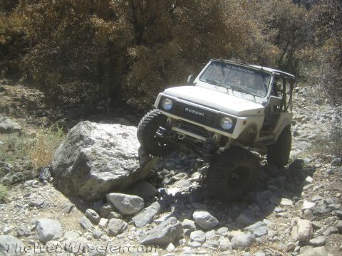 1987 Suzuki Samurai - A white 1987 Suzuki Samurai tackles a challenging rocky trail, demonstrating its off-road capabilities.