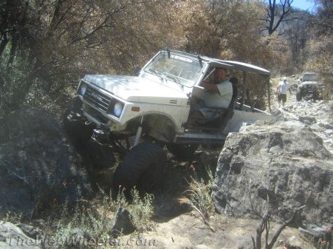 1987 Suzuki Samurai - A white Suzuki Samurai is shown navigating a difficult, rocky trail with a driver and passenger inside. Another vehicle is seen in the back…