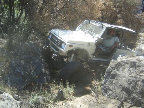 1987 Suzuki Samurai - A white 1987 Suzuki Samurai is shown off-roading on a rocky trail, with its front-right wheel lifted.