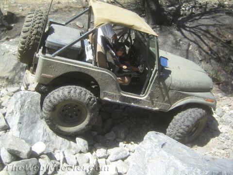 1987 Suzuki Samurai - Olive green Jeep CJ-7 tackling a rocky trail with a child in the passenger seat.