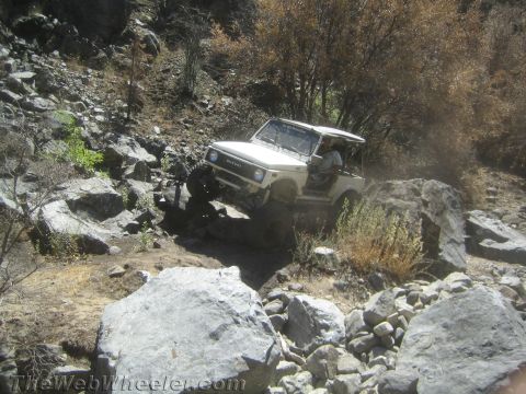 1987 Suzuki Samurai - A white Suzuki Samurai is shown navigating a challenging, rocky off-road trail.